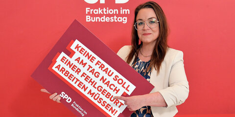 Unsere Abgeordnete Sarah Lahrkamp, hält ein Schild mit der Aufschrift „Keine Frau soll am Tag nach einer Fehlgeburt arbeiten müssen!"