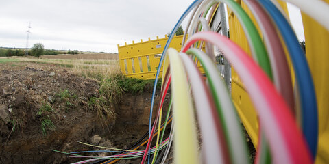 Leerrohre für Glasfaserleitungen für schnelles Internet liegen an einer Landstraße bei einem Dorf in der Baugrube.
