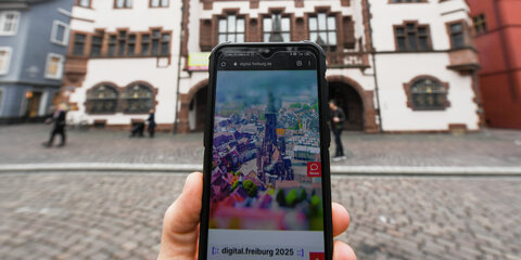 Auf einem Smartphone vor dem Rathaus ist die Webseite „Digital.freiburg.de“ geöffnet.
