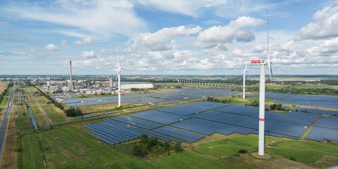 Windkraftanlagen drehen sich bei leichter Bewölkung in einem Solarpark.