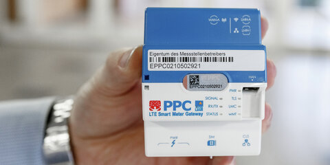 Eine Hand hält ein Smart-Meter-Gateway zur Übertragung der Daten von digitalen Stromzählern.