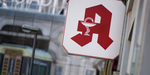 Ein Schild mit dem Apotheken-Logo hängt über dem Eingang zu einer Apotheke.