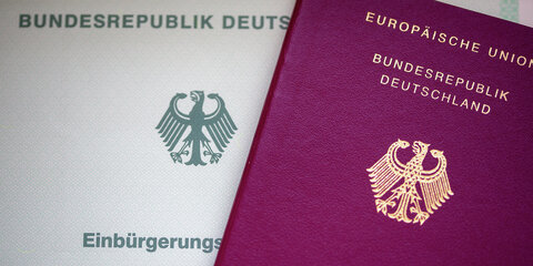 Eine Einbürgerungsurkunde der Bundesrepublik Deutschland (l) und ein deutscher Reisepass liegen auf einem Tisch.