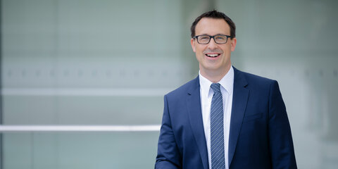 Sören Bartol steht lächelnd auf einem Balkon im Reichstagsgebäude und schaut frontal in die Kamera
