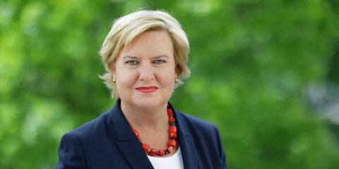 Eva Högl steht auf einem Balkon mit grünen Bäumen im Hintergrund und schaut lächelnd in die Kamera.