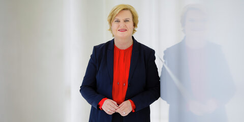 Eva Högl steht neben einer spiegelnden weißen Wand und schaut lächelnd in die Kamera.