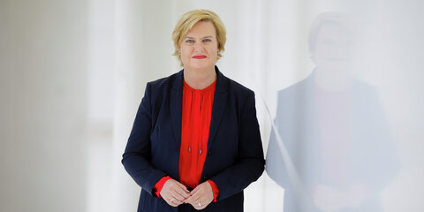 Eva Högl steht neben einer spiegelnden weißen Wand und schaut lächelnd in die Kamera.