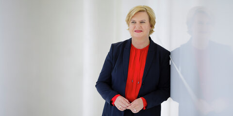 Eva Högl steht neben einer spiegelnden weißen Wand und schaut lächelnd in die Ferne.
