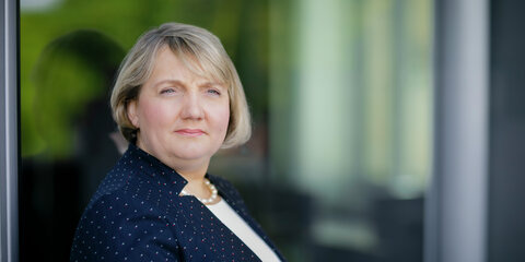 Katja Mast steht an eine Fensterscheibe angelehnt und schaut nachdenklich in die Ferne