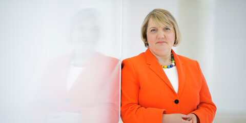Katja Mast steht neben einer Wand und schaut nachdenklich in die Kamera