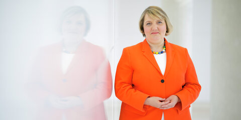 Katja Mast steht neben einer Wand und schaut freundlich in die Kamera