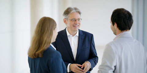Achim Post im Gespräch mit zwei Personen, die ihm links und rechts frontal gegenüberstehen.