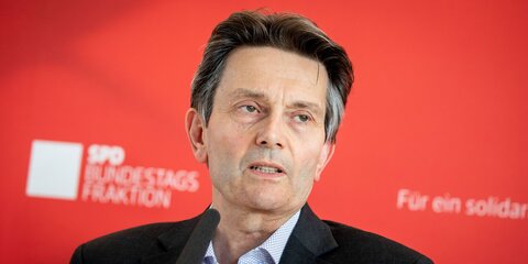 Rolf Mützenich steht vor einer roten Pressewand und gibt eine Pressestatement.