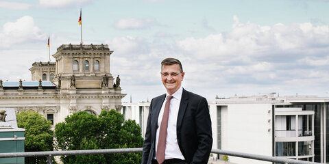 Foto von Martin Rabanus, der lächelnd in die Kamera schaut, im Hintergrund ist u. a. das Reichstagsgebäude zu sehen.