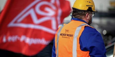 Ein Teilnehmer der Protestaktion gegen den drohenden Arbeitsplatzabbau beim Kreuzfahrtschiffbauer Meyer Werft steht mit einer Flagge vor dem Werfgelände.