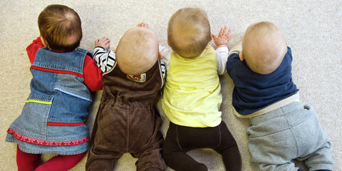 Vier Babys krabbeln in einer Kindertagesstätte auf dem Teppich.
