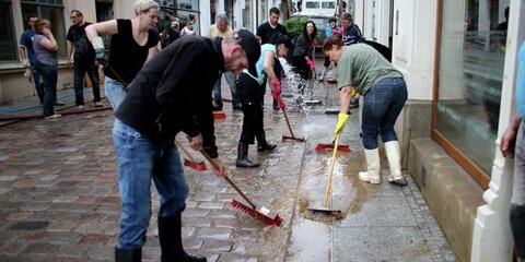Das Foto zeigt Hochwasserschäden im Jahr 2013. Bürgerinnen und Bürger putzen den Schlamm auf der Straße weg.