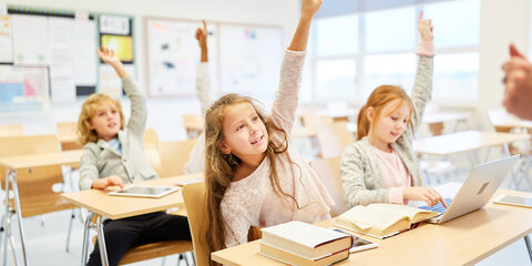 Junge Schüler sitzen in einem Klassenraum an der Schulbank und melden sich.