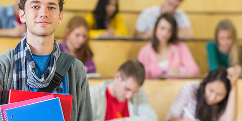 Porträt eines lächelnden Mannes mit Studenten, die im Hörsaal sitzen