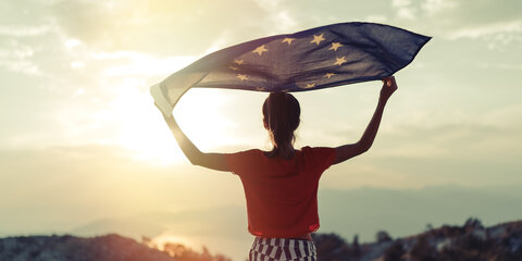  Eine junge Frau steht auf einem Berg und winkt mit der Flagge der Europäischen Union.