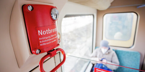 Ein Fahrgast mit Mund-Nasen-Schutz sitzt in einer Berliner S-Bahn hinter der Notbremse.