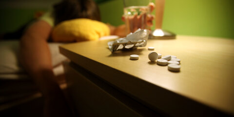 Ein Jugendlicher liegt in einem Bett, auf seinem Nachtisch sind Tabletten.
