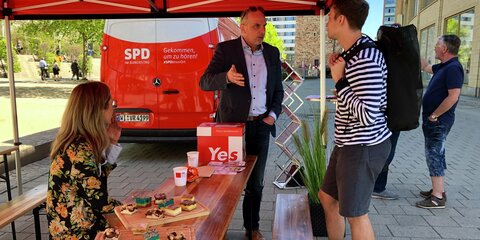 Detlef Müller steht unter einem roten Pavillondach und spricht mit einem jungen Mann.