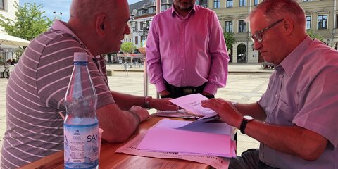 Thomas Jurk sitzt auf einem Marktplatz mit zwei Bürgern an einem Tisch und unterhält sich.