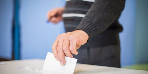 Eine Person wirft einen Umschlag in eine Wahlurne.
