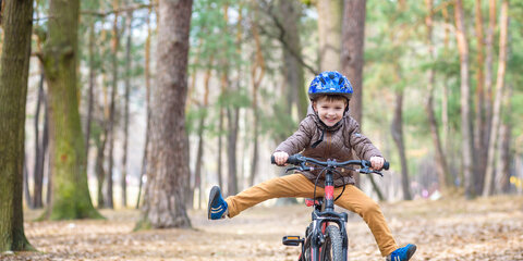 Glücklicher Junge hat Spaß im Herbstwald mit seinem Fahrrad