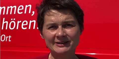 Daniela Kolbe steht vor dem roten Tourbus und spricht in die Kamera.