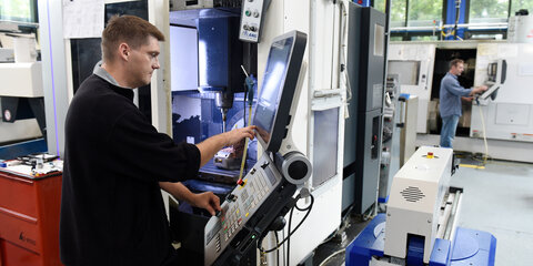 Ein Mitarbeiter arbeitet an der Steuereinheit einer Fräsmaschine.