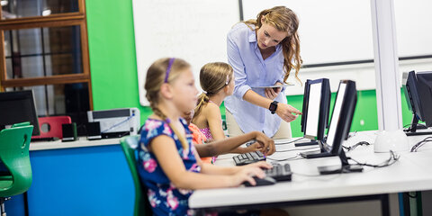 Eine Lehrerin, die ihre Schülerinnen am Computer unterrichtet