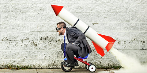 Businessmann auf Dreirad mit Rakete auf dem Rücken