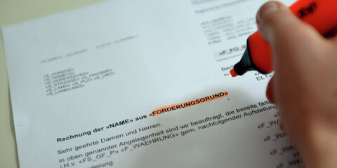 Eine Mitarbeiterin sitzt bei einem Inkasso-Unternehmen an ihrem Schreibtisch und hält ein Formular in der Hand.