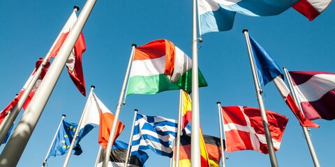Mehrere europäische Flaggen wehen vor blauem Himmel.