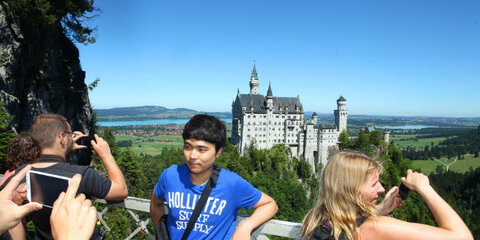 Touristen stehen auf der Marienbrücke bei Hohenschwangau (Bayern) vor dem Schloss Neuschwanstein und posieren für ein Erinnerungsfoto. 