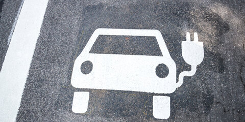 Ein kleines weißes Auto ist als Parkzeichen für Elektroautos auf dem Asphalt markiert.