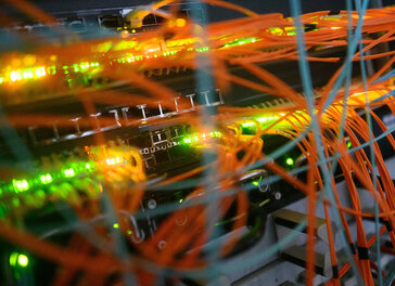 Blick auf einen Serverschrank mit blinkenden Lampen und Kabeln.