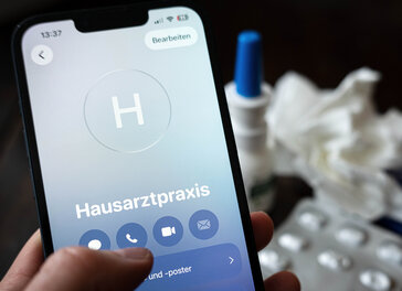 Eine Person hält ein Smartphone in der Hand und ruft eine Hausarztpraxis an.