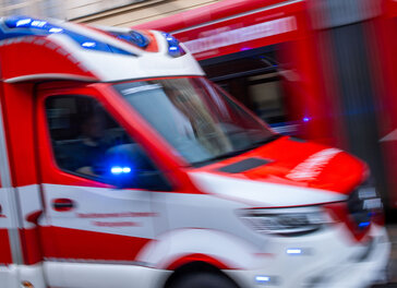 Ein Rettungsfahrzeug ist mit Blaulicht auf einer Straße in der Innenstadt unterwegs.